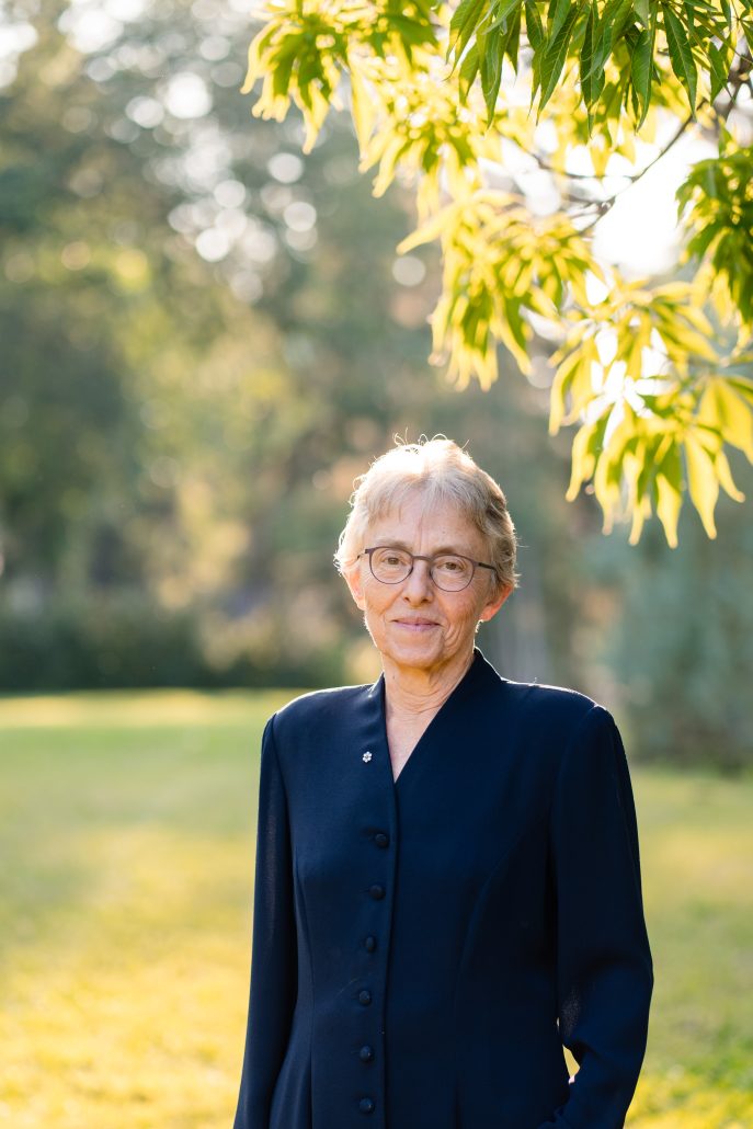Women in a blue blazer standing out in a park with trees illuminated by the sunlight.