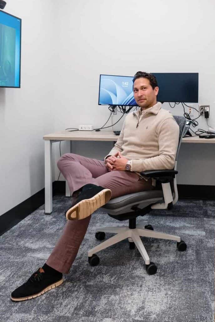 Allan Black sits in a chair in the virtual centre, with computer screens behind him.
