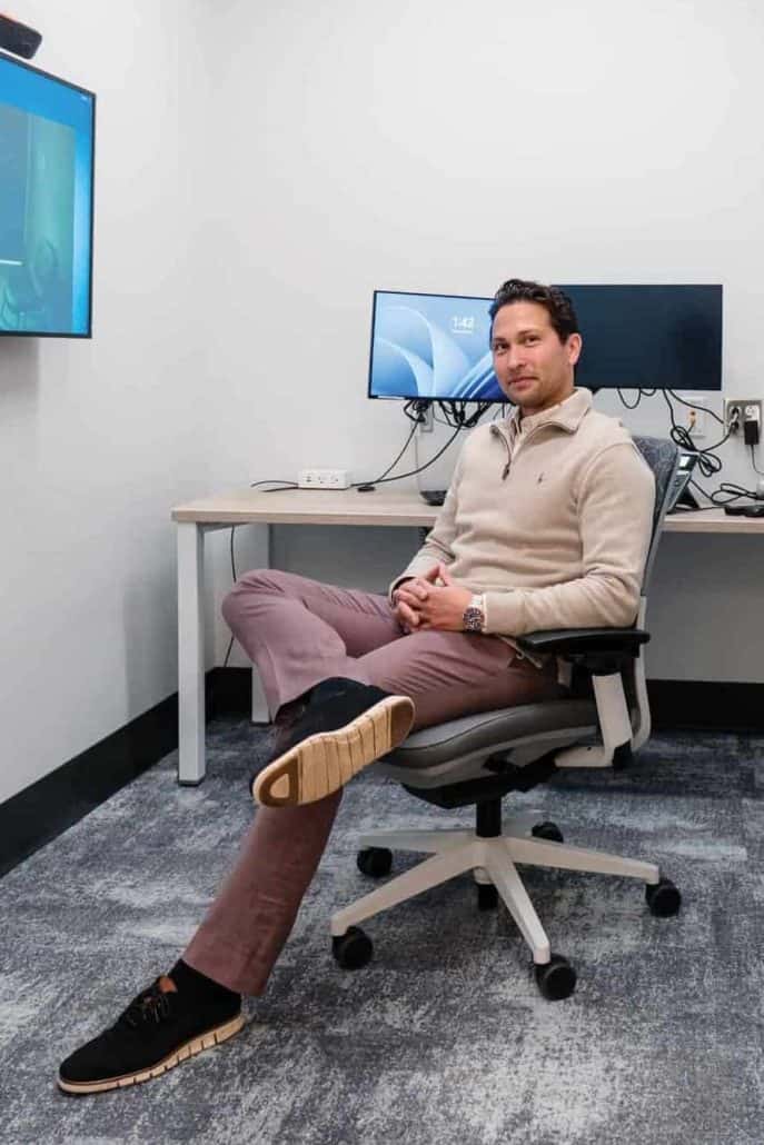Allan Black sitting on a chair with computers behind him.
