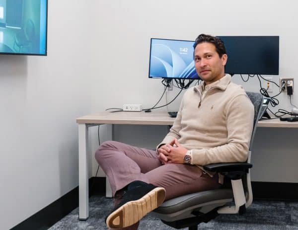 Allan Black sitting on a chair with computers behind him.