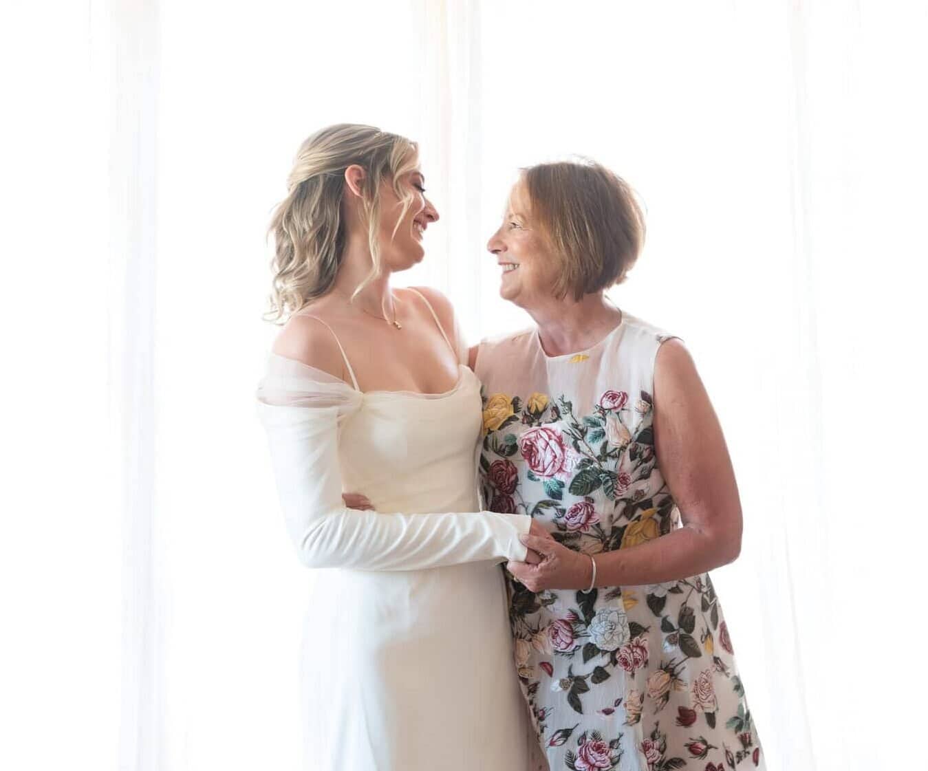 Mother and daughter look at each lovingly on the daughter's wedding day. 