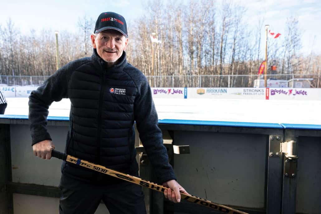 Barrie Stafford stands in front of an ice rink, holding a hockey stick.