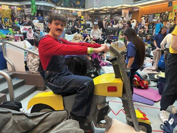A student dressed as Mario sits on a stationary bike.