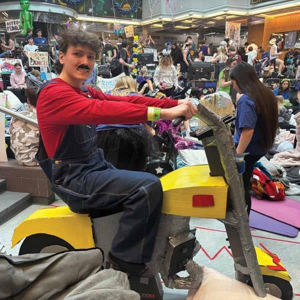 A student dressed as Mario sits on a stationary bike.