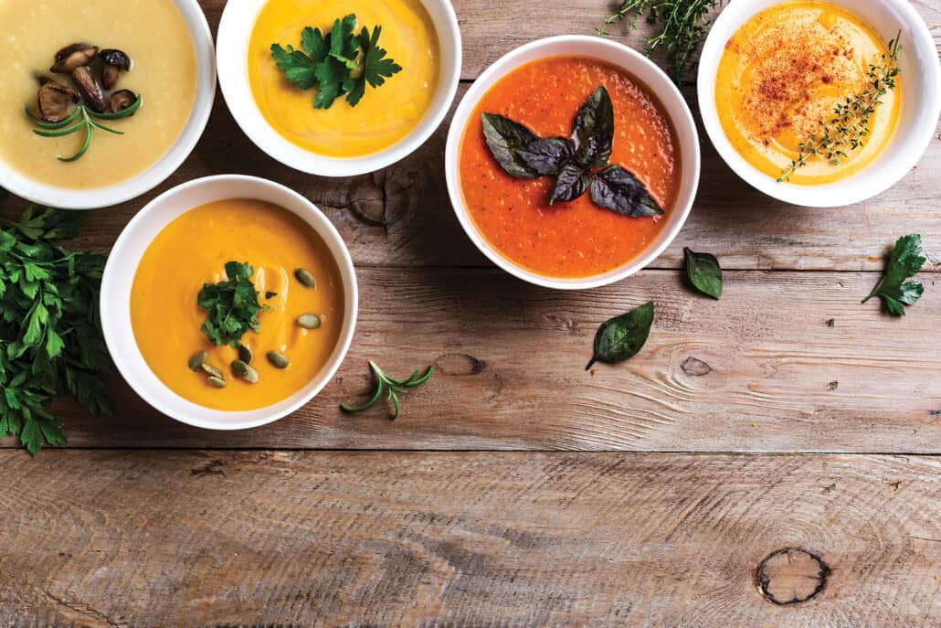 Top view of several colourful bowls of soup on a table.