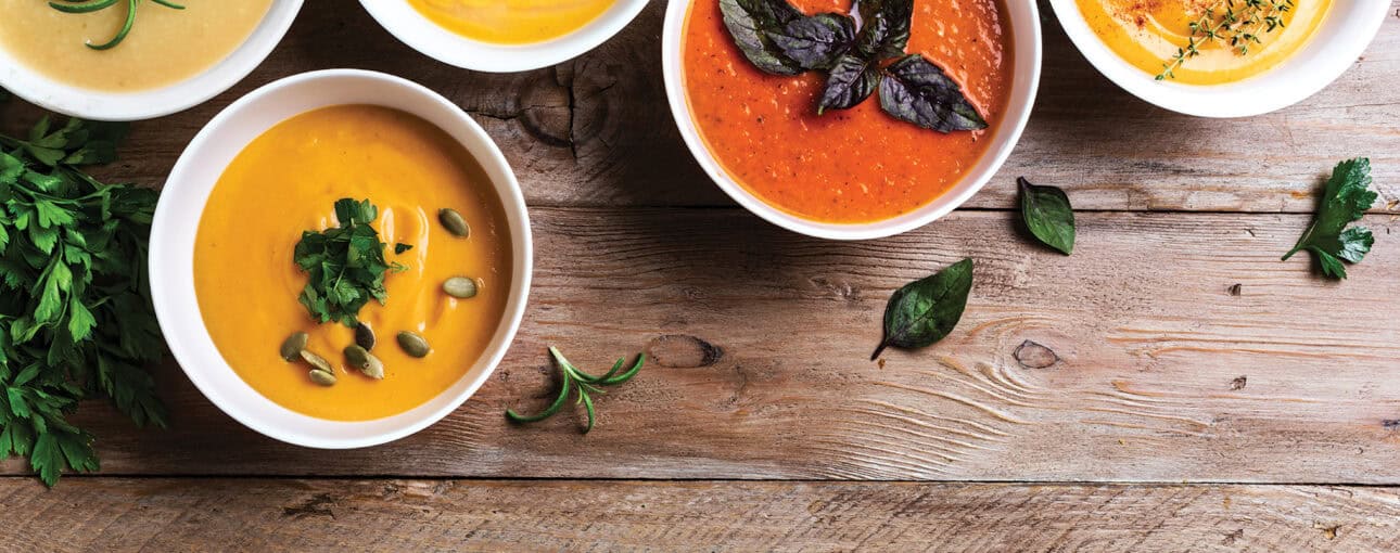 Top view of several colourful bowls of soup on a table.