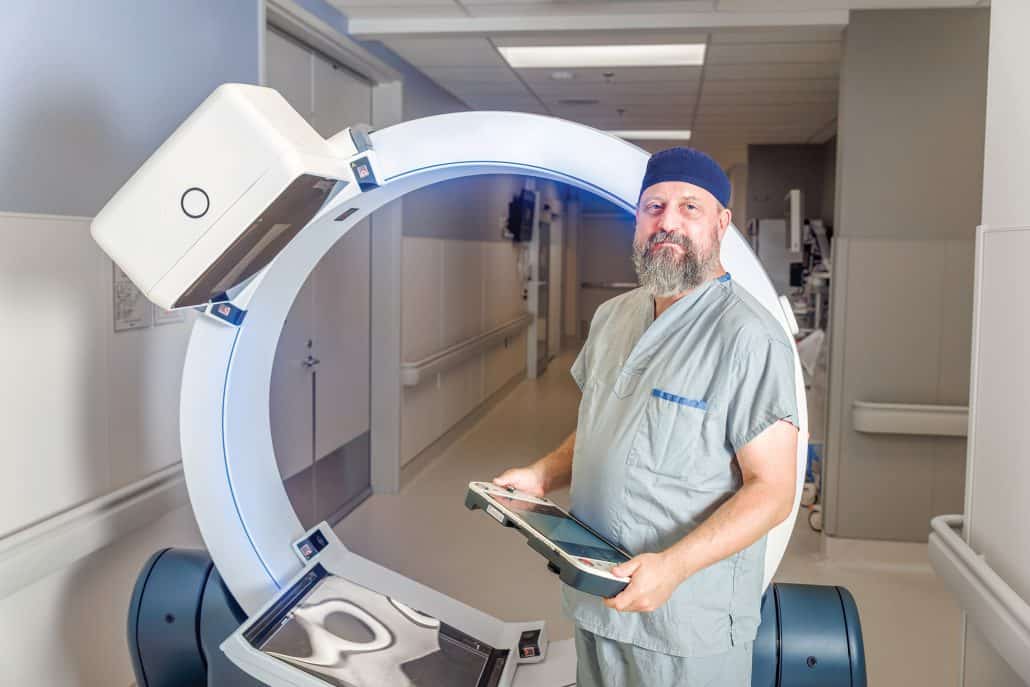 Dr. Tyler Meyer in scrubs standing in front of a a mobile ring CT scanner.