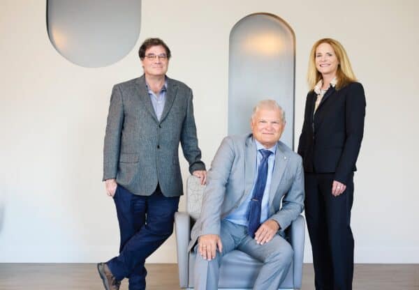 A picture of three medical professionals. Two stand while the third sits in a chair between them.