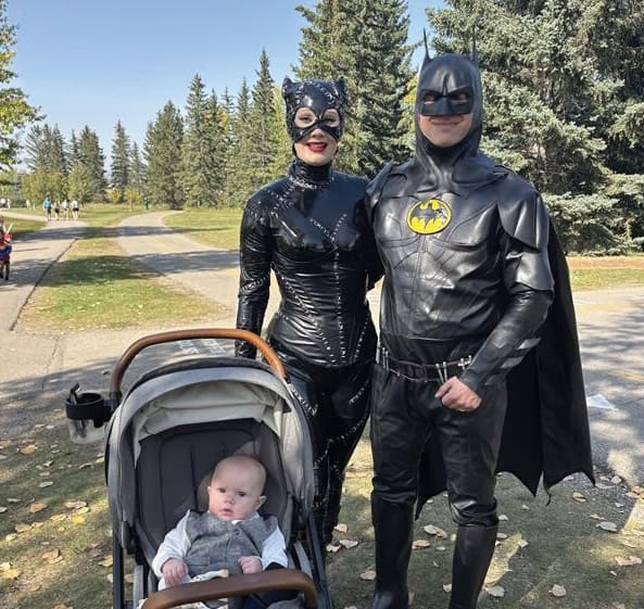 Mom and dad dressed up as Batman and Catwoman with their baby in a stroller.