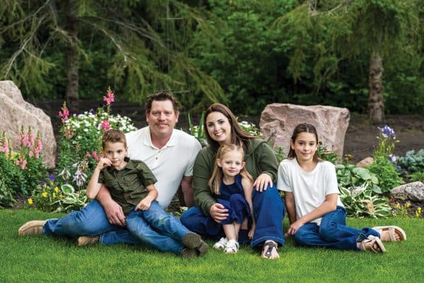 Family picture featuring mom, dad and three kids all sitting on the grass.