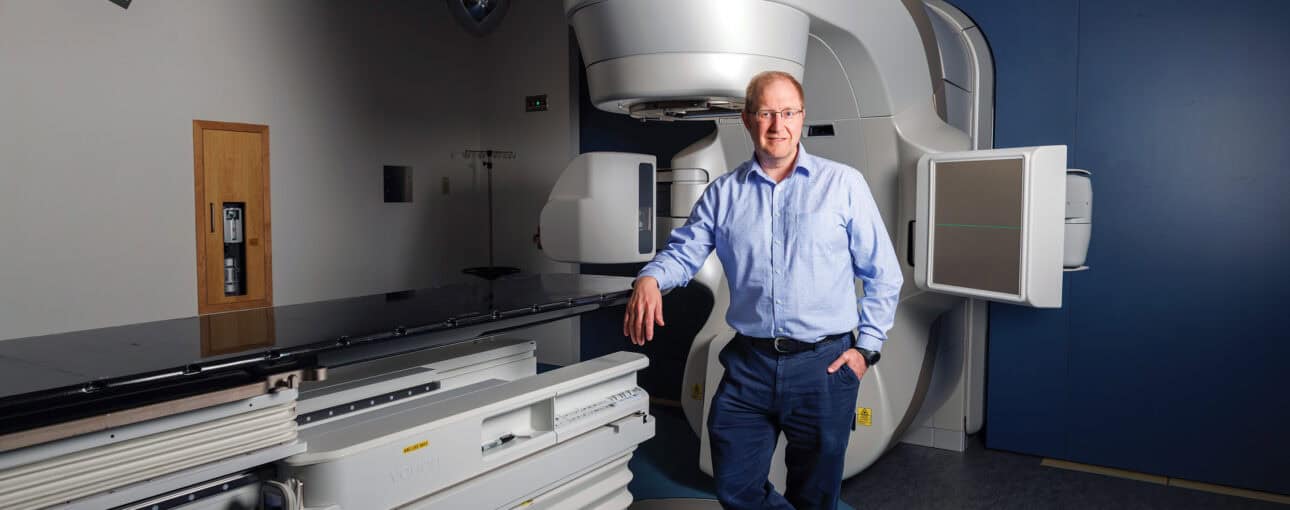 Man stands next to a linear accelerator machine.
