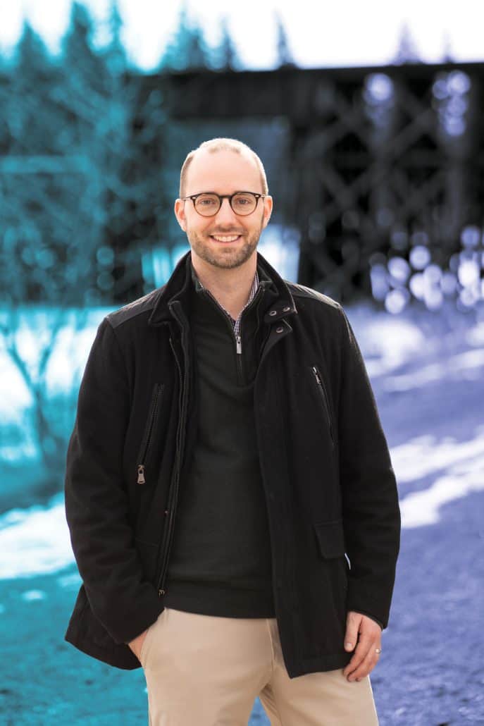 Man stands outside smiling with his hand in his pocket.
