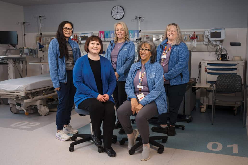 A team of five women in blue jackets smile at the camera.