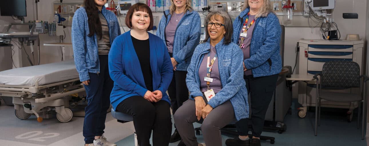 A team of five women in blue jackets smile at the camera.