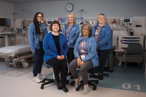 A team of five women in blue jackets smile at the camera.