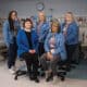 A team of five women in blue jackets smile at the camera.