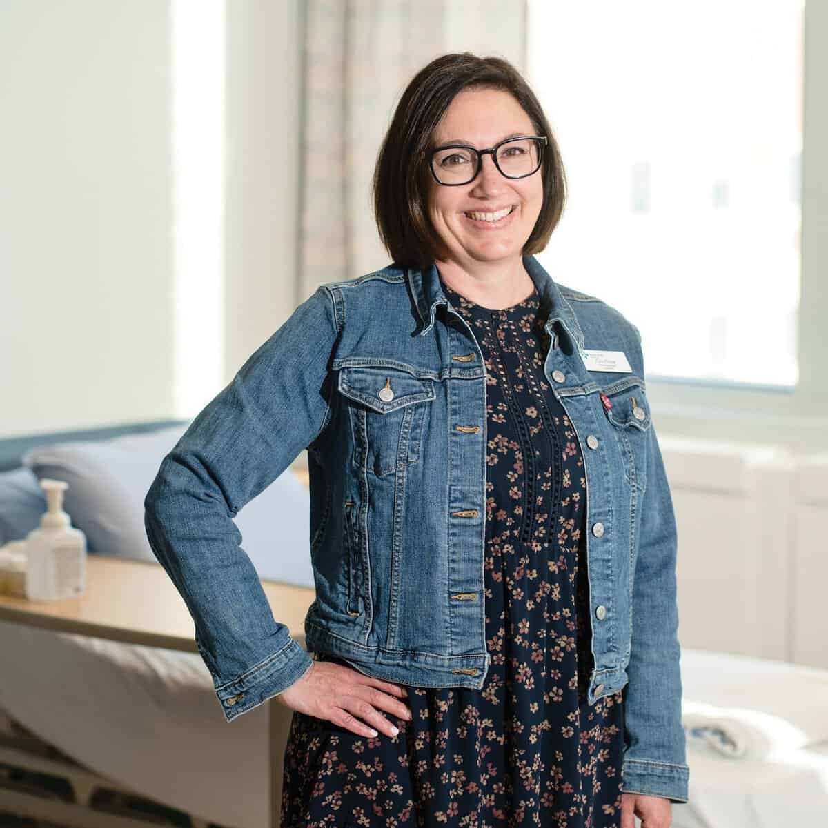 Woman in a jean jacket with a hand on her hip, smiling at the camera