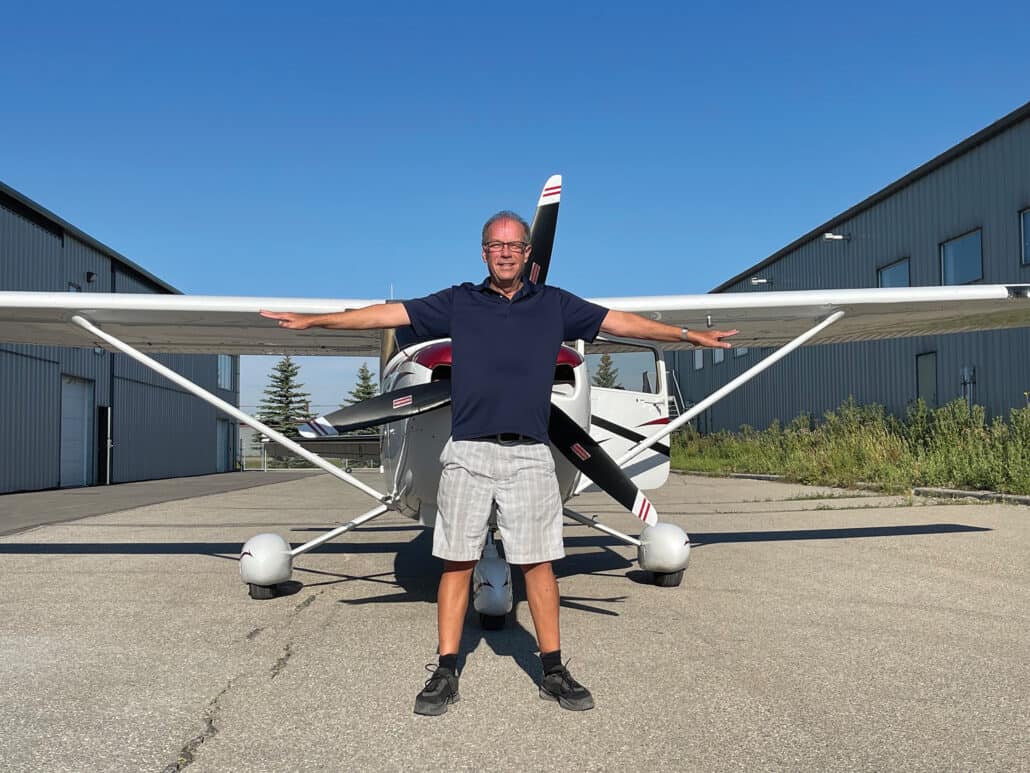 A man stands in front of an airplane with his arms stretched out.