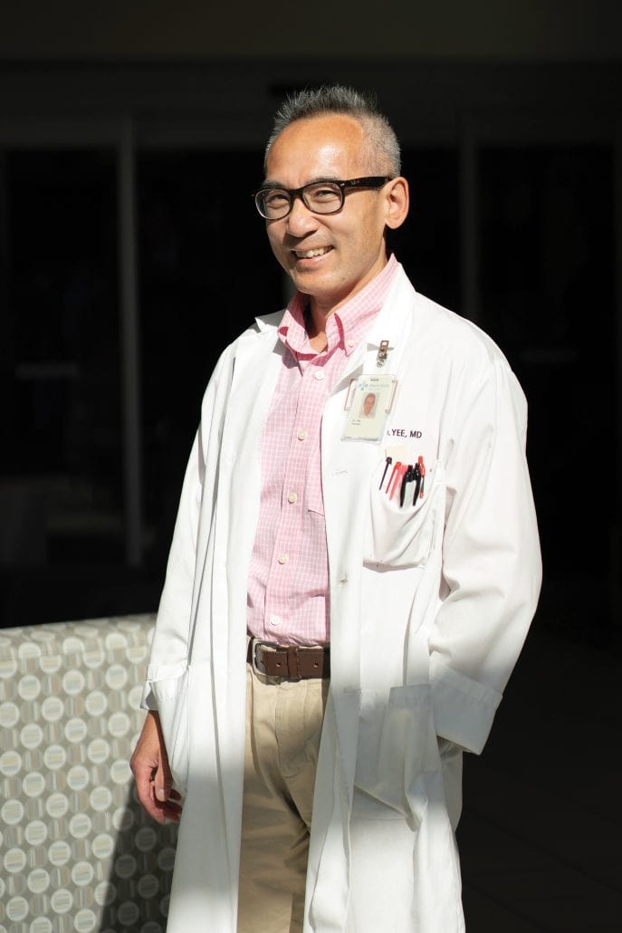 Leading the way. 4 Man in a white lab coat and pink shirt looking at the camera while standing in sunlight.