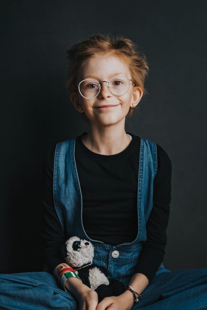 Young girl smiles at the camera while holding a stuffed animal.