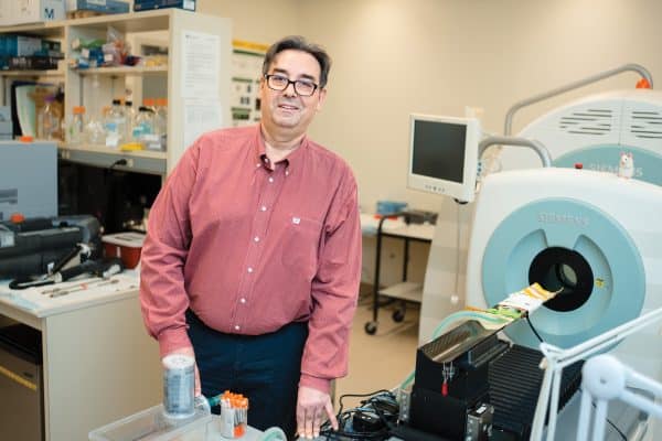 Dr. Frank Wuest in a pink button-shirt standing next to imaging equipment.