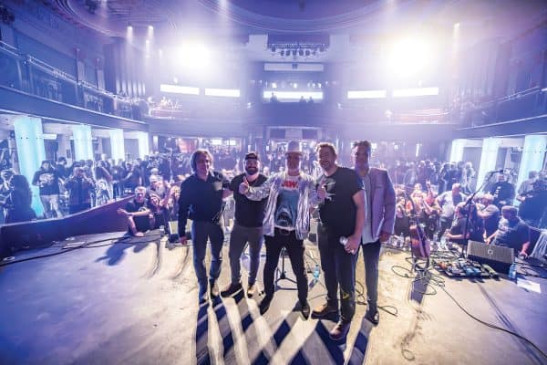 Band stands on stage with lights the crowd behind them.