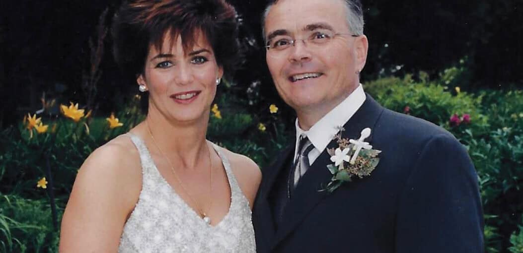 Sharon McMinn and Jeff Goin stand together, in a white dress and suit, on their wedding day.