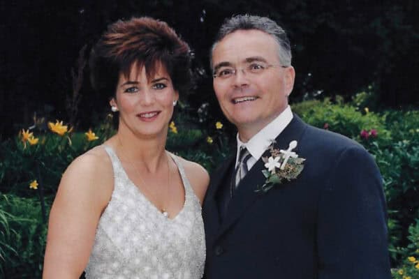 Sharon McMinn and Jeff Goin stand together, in a white dress and suit, on their wedding day.