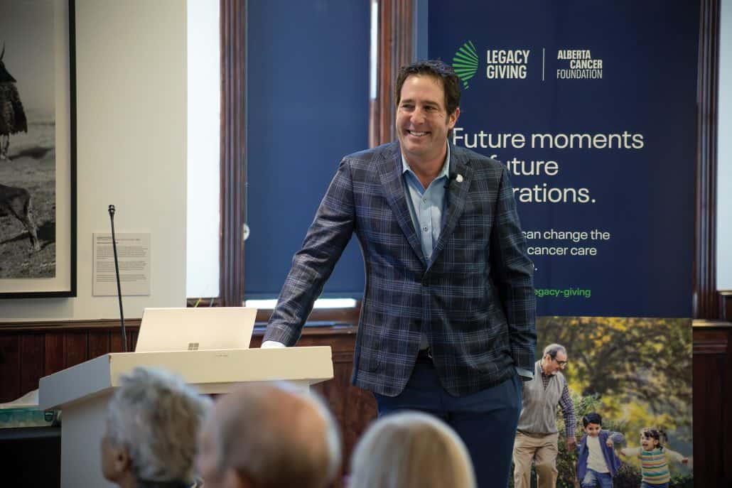 Jeff Evans wears a suit and stands in front of a crowd, smiling, with his hand on the podium.