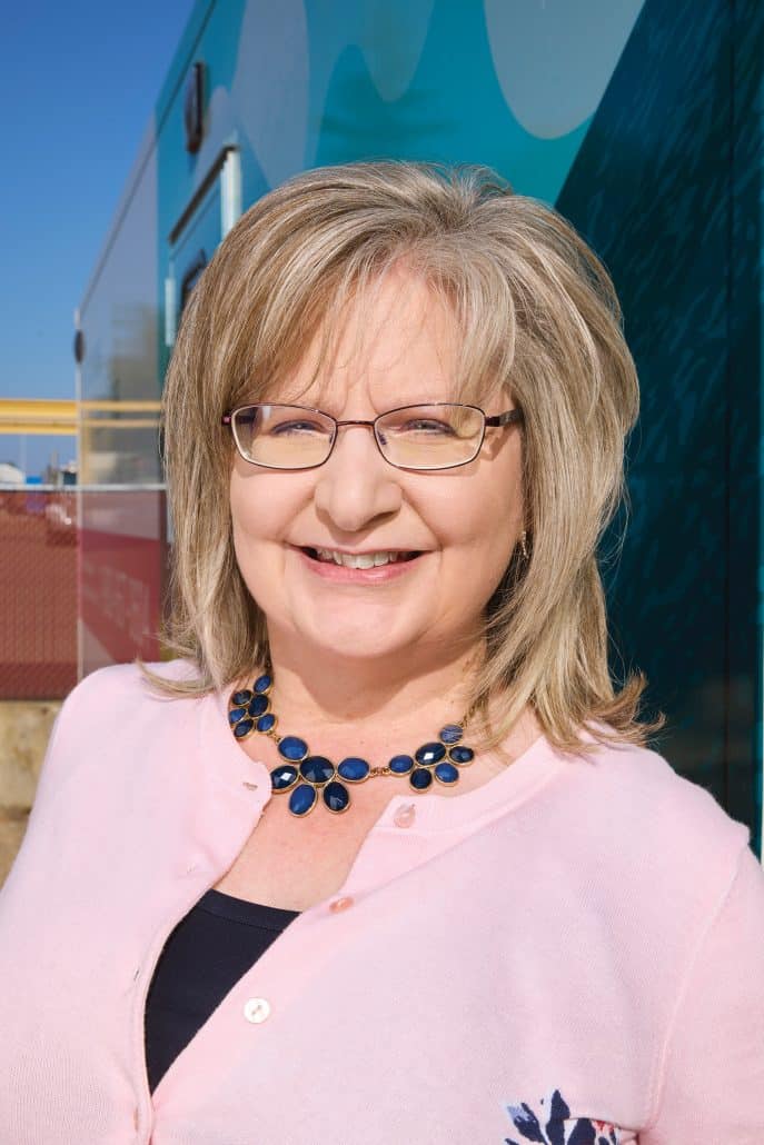 True calling. 2 Portrait image of a woman smiling, wearing pink and a flowery necklace.