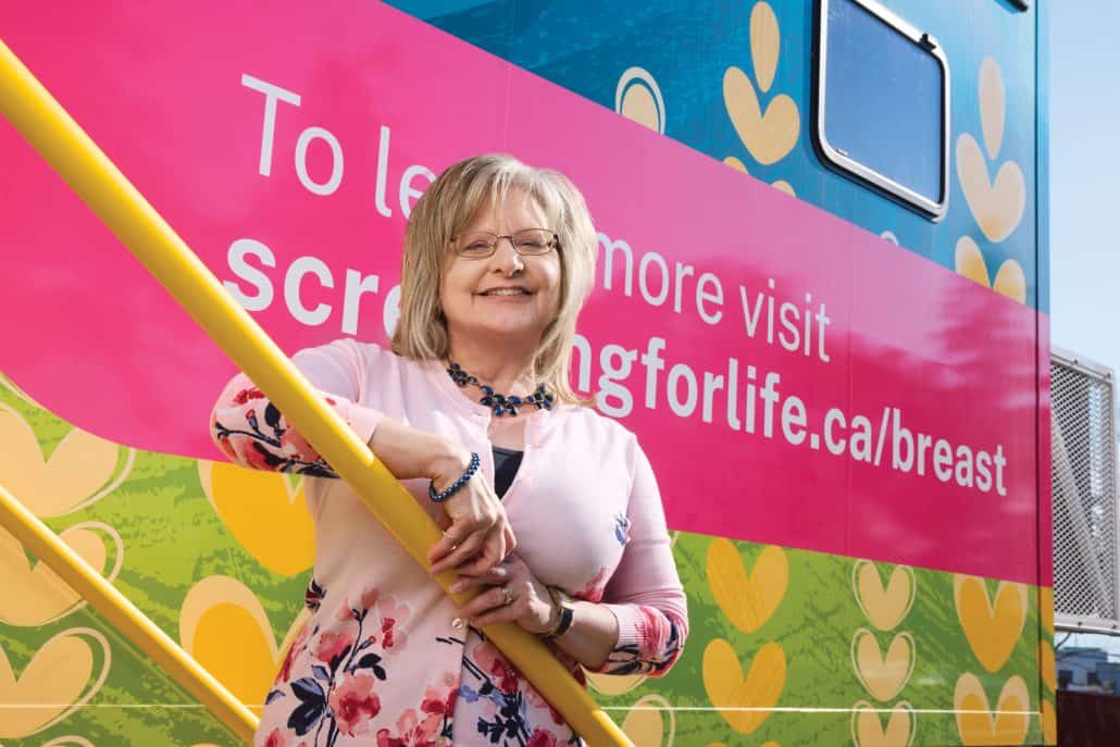 True calling. 1 Woman standing in front of a mobile screening unit, smiling at the camera.
