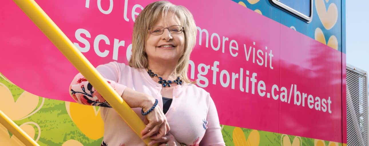Woman standing in front of a mobile screening unit, smiling at the camera.