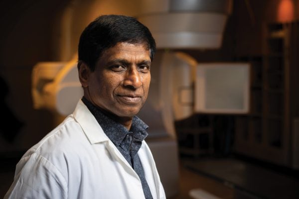 Doctor in white coat looking at the camera and standing in front of a radiation machine.