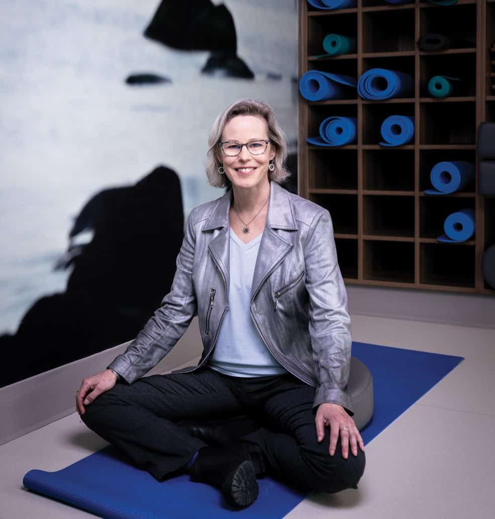 Dr. Linda Carlson sitting on a  blue yoga mat with her legs crossed.
