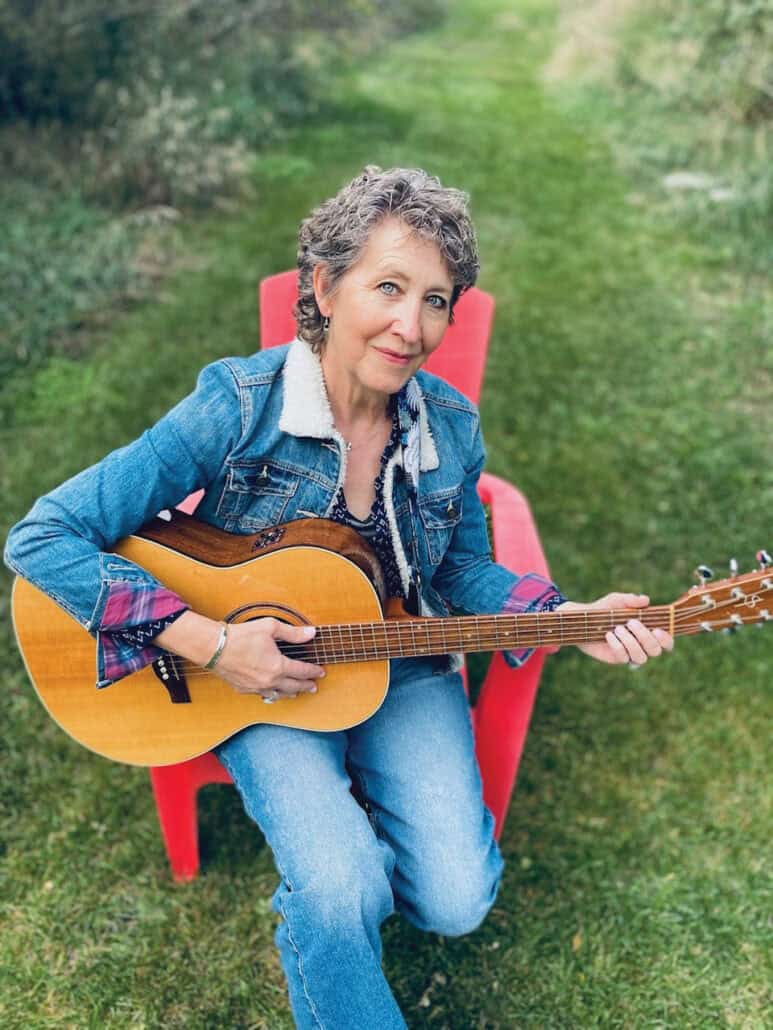 Lucinda Warnock sits in a red chair, holding her guitar. 