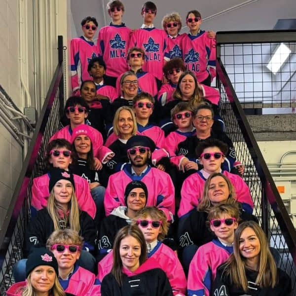 Several young adults sit in a stairwell together, wearing pink jerseys and sunglasses.