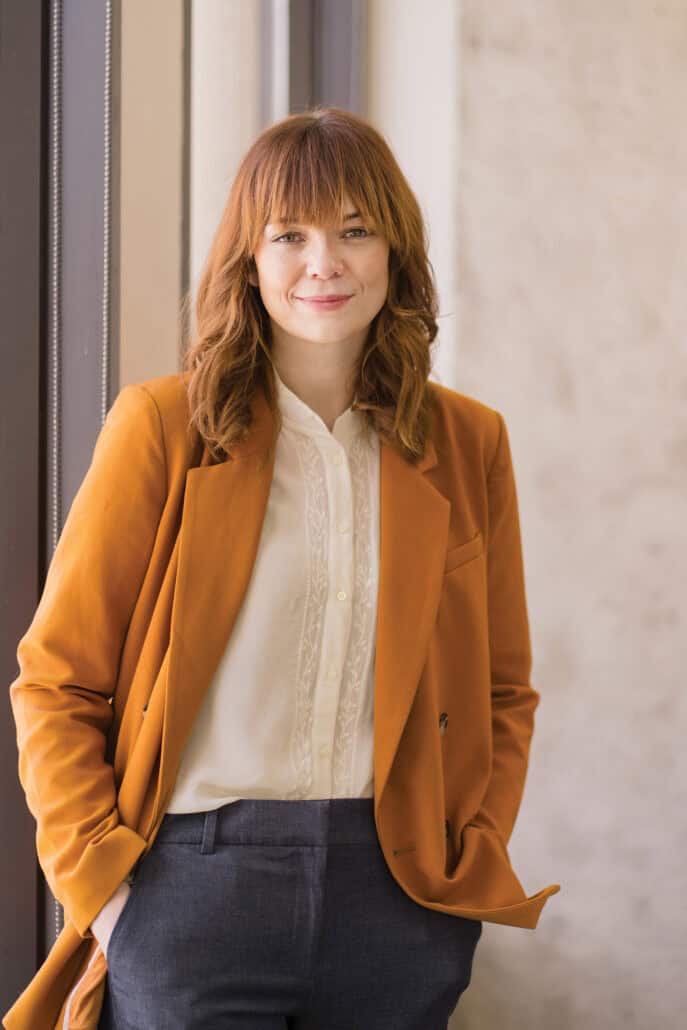 Maeve Wickham standing in her burnt orange blazer, with her hands in her pocket.
