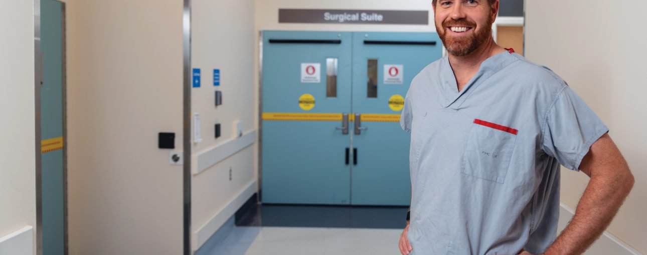 Doctor in scrubs standing in a hospital hallway.