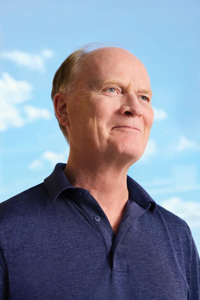 Man smiles off into the distance with a blue sky behind him.