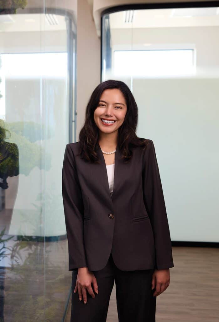 Woman in a black blazer stands smiling at the camera.