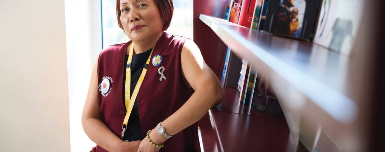 Woman leans up against a burgundy book shelf.