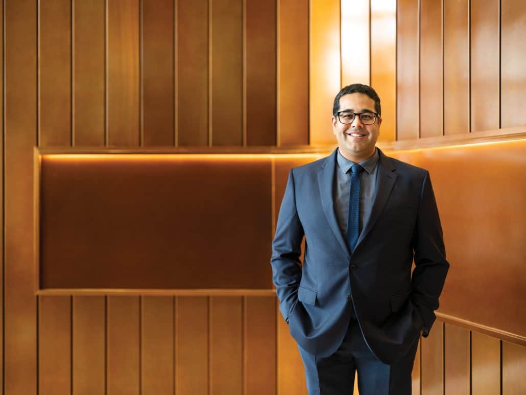 Man in a blue suit against a brown wall.
