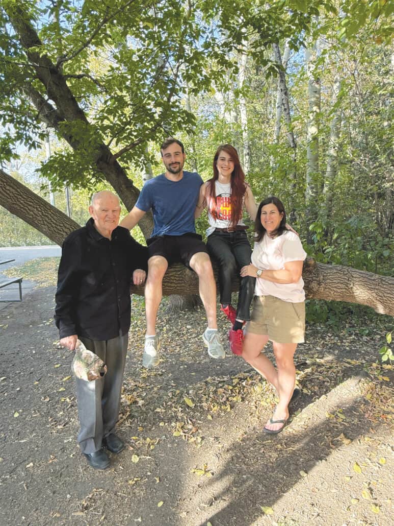 Turning tragedy into hope 1 Peter Kossowan stands next to a large tree branch which his grandson and granddaughter are sitting on, along with his daughter on the other side.