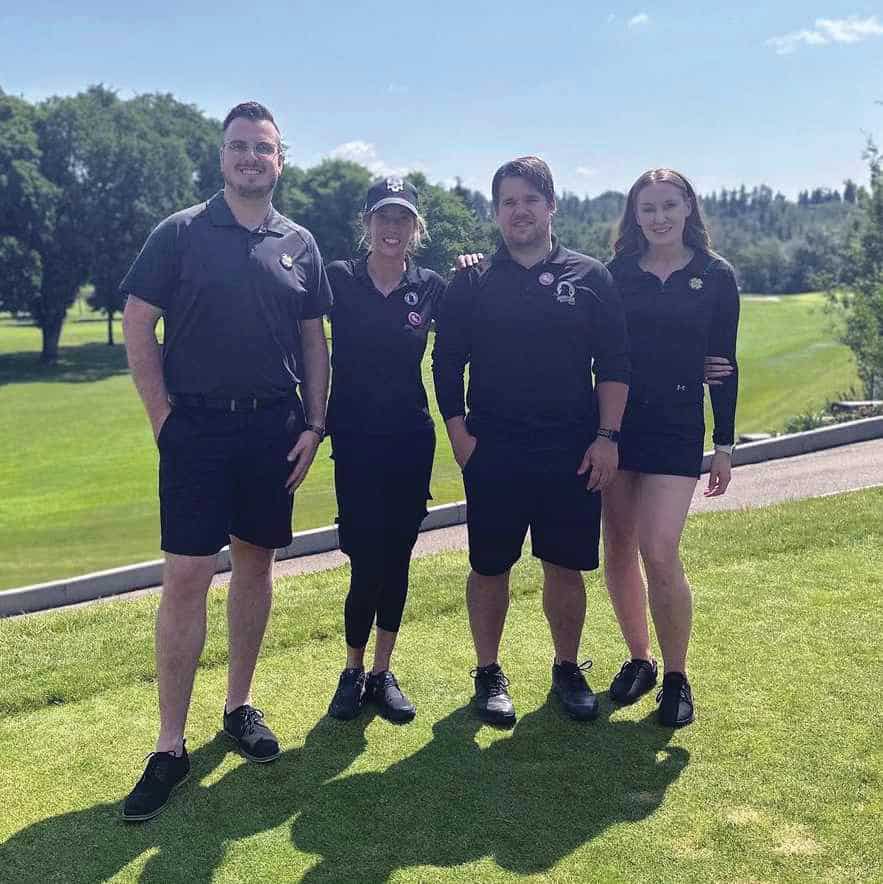Four people stand on a gold course.