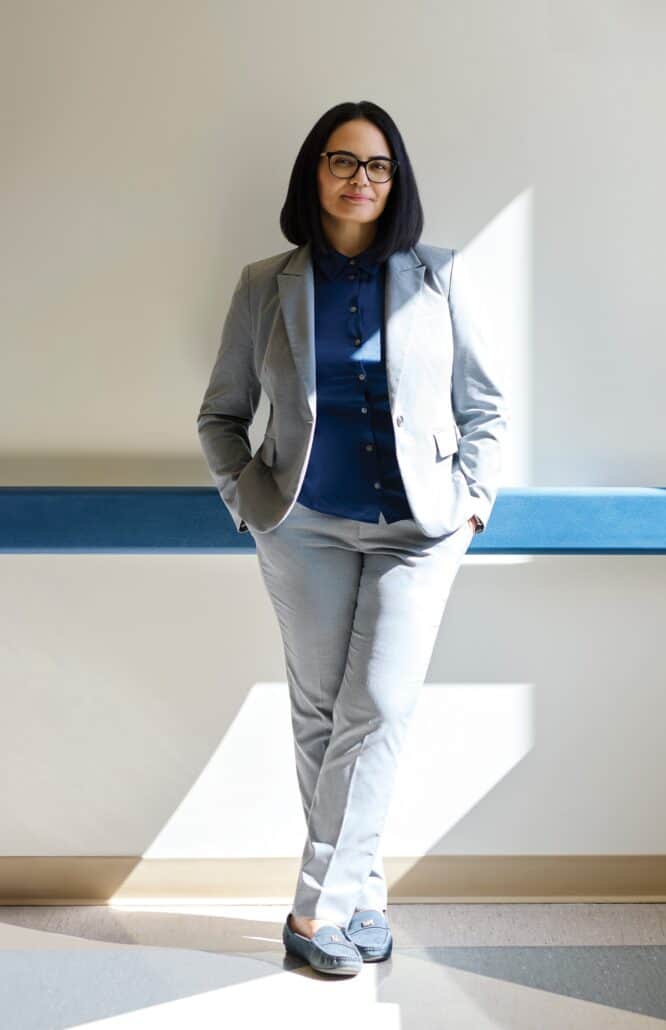 Woman leans up against a wall with her hands in her pockets.
