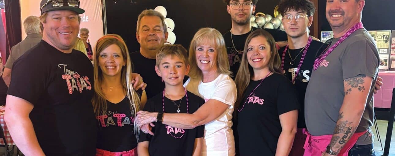 A family in matching black t-shirts and some wearing pink shorts pose together during a fundraiser.