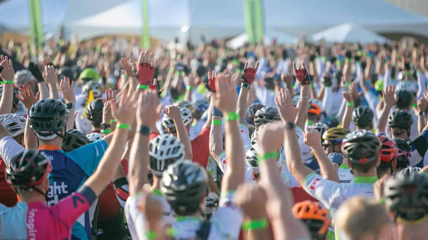 A sea of cyclists celebrating at the opening ceremony, all with their hands up. 