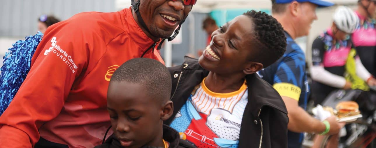 The pedal power of many 3 Tendai Mashonganyika in a helmet and riding sunglasses alongside his family looking at him lovingly while celebrating.