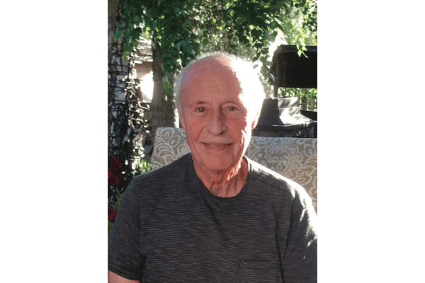 Elderly man smiling at the camera while sitting outside.